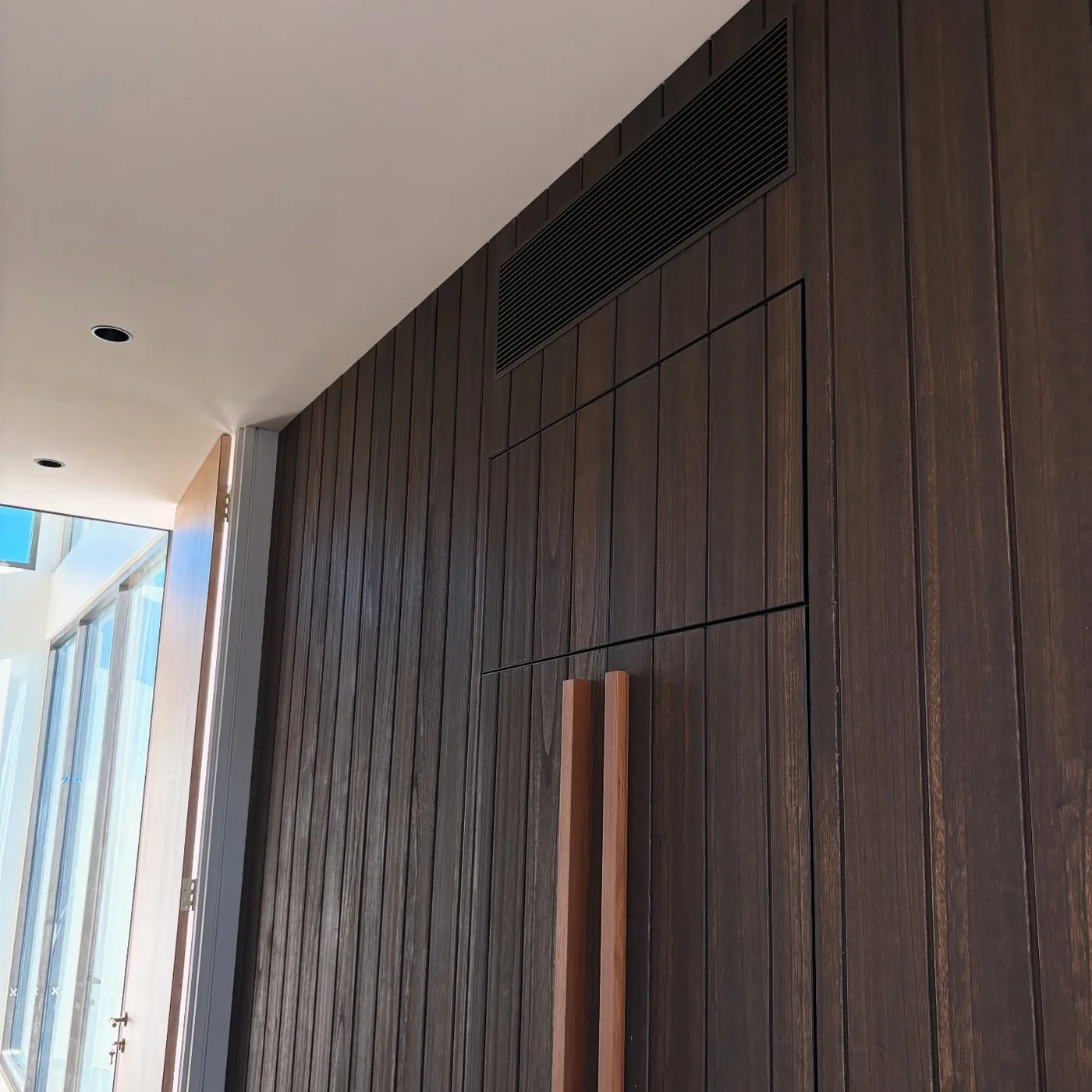 Linear grille set flush into a dark timber joinery wall